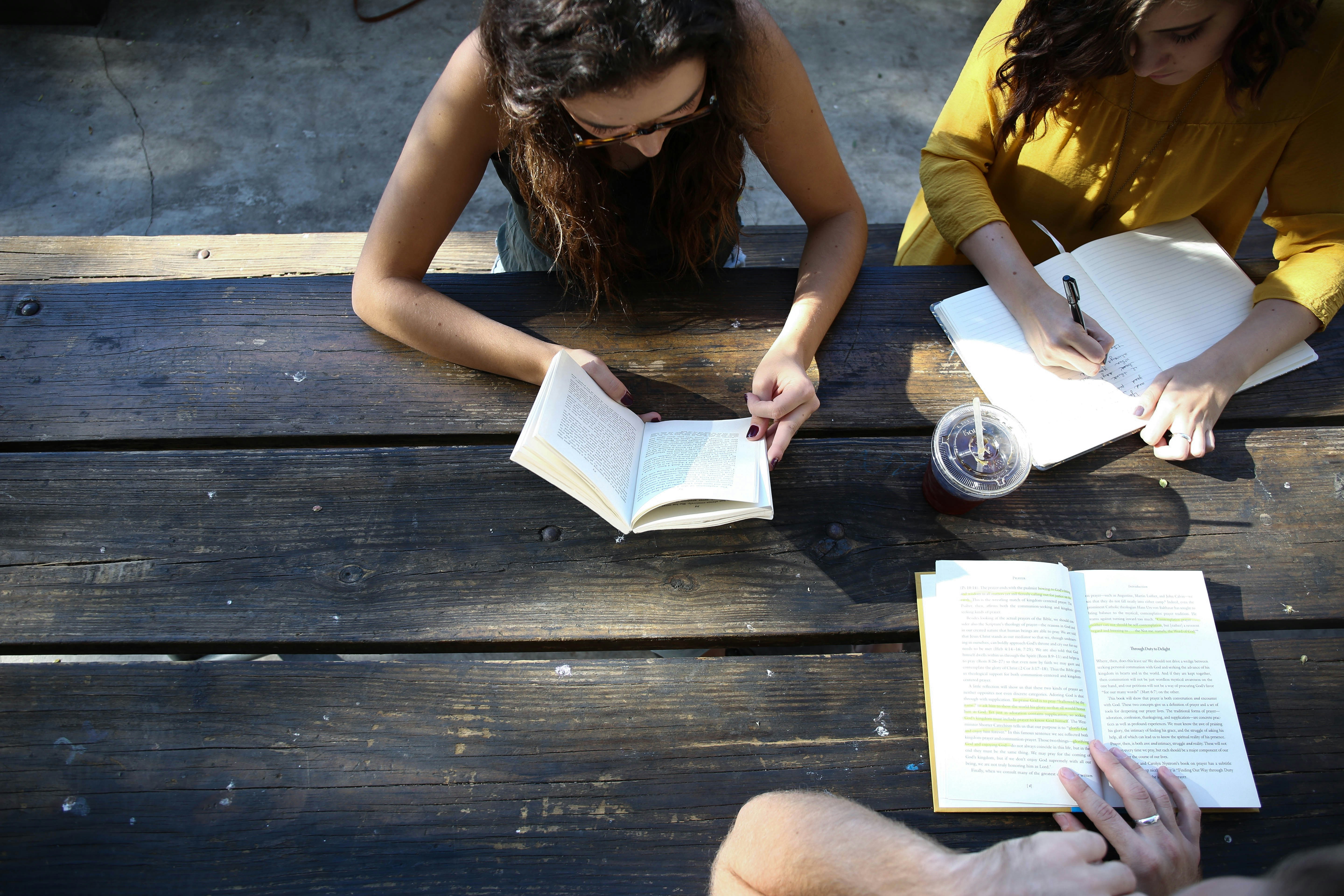 Three people sat at an outdoor table writing and reading