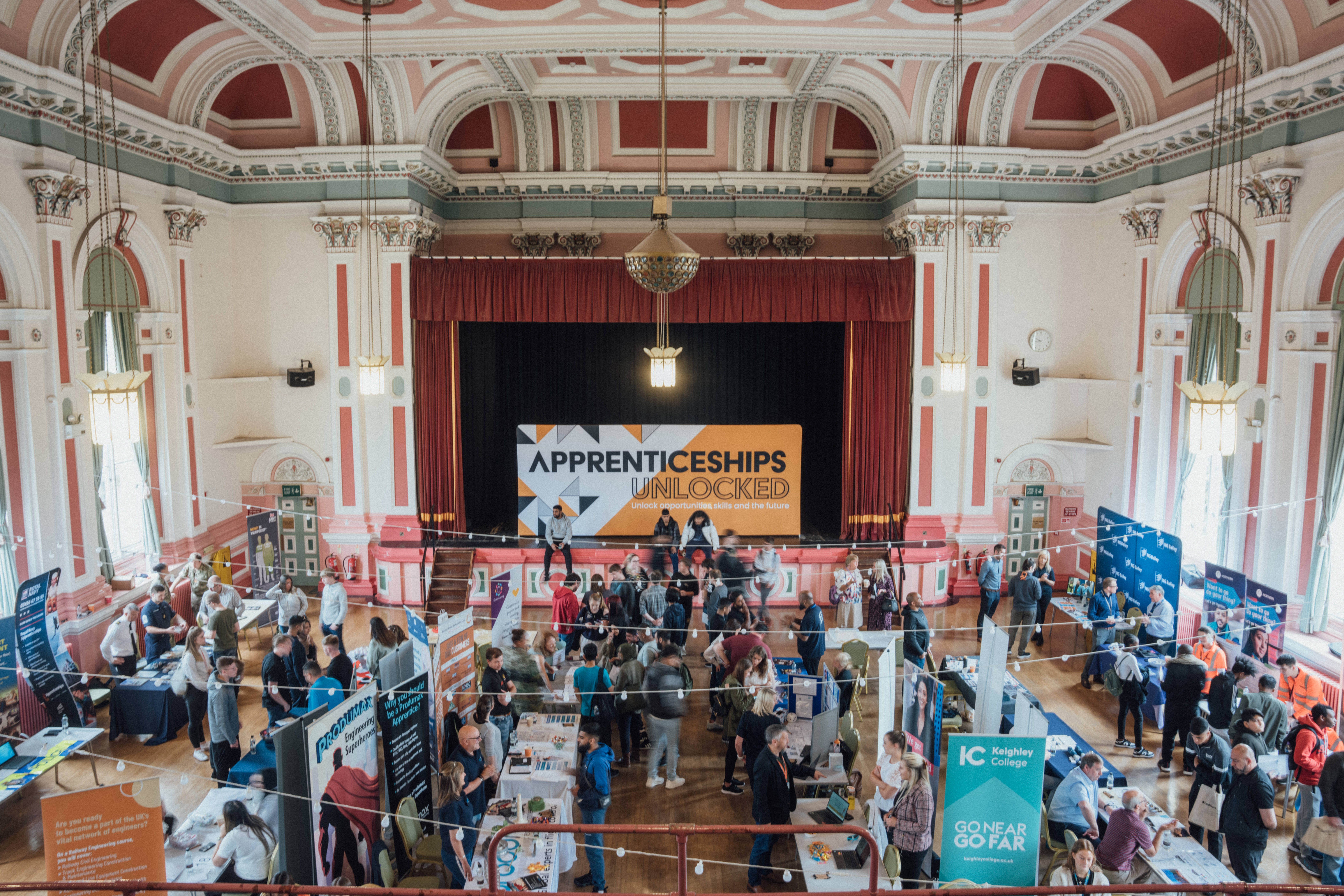 A large hall with stalls, banner stands and lots of people.  The banner at the back reads Apprenticeships Unlocked