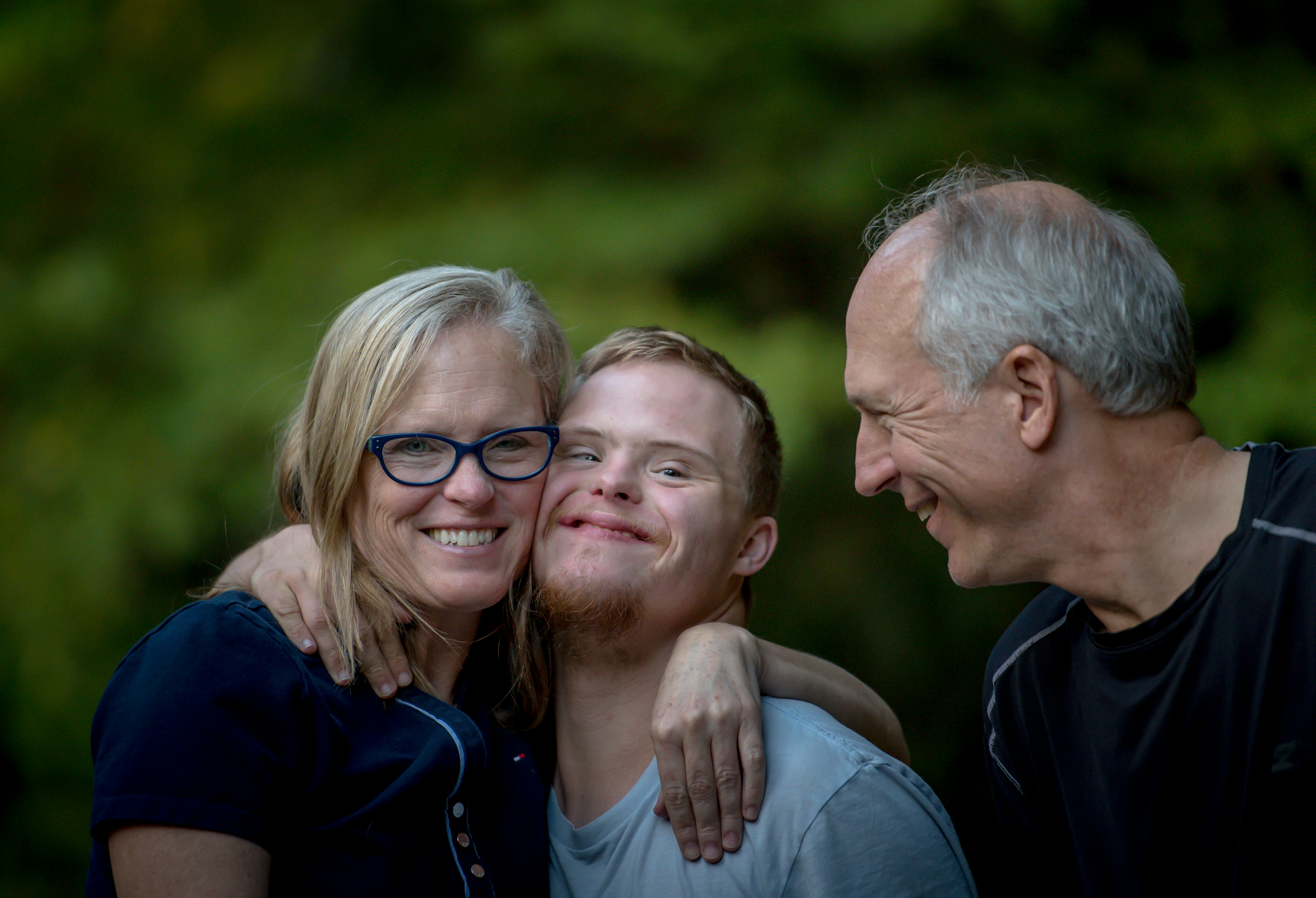 An older man and woman hugging a younger man who has Downs syndrome