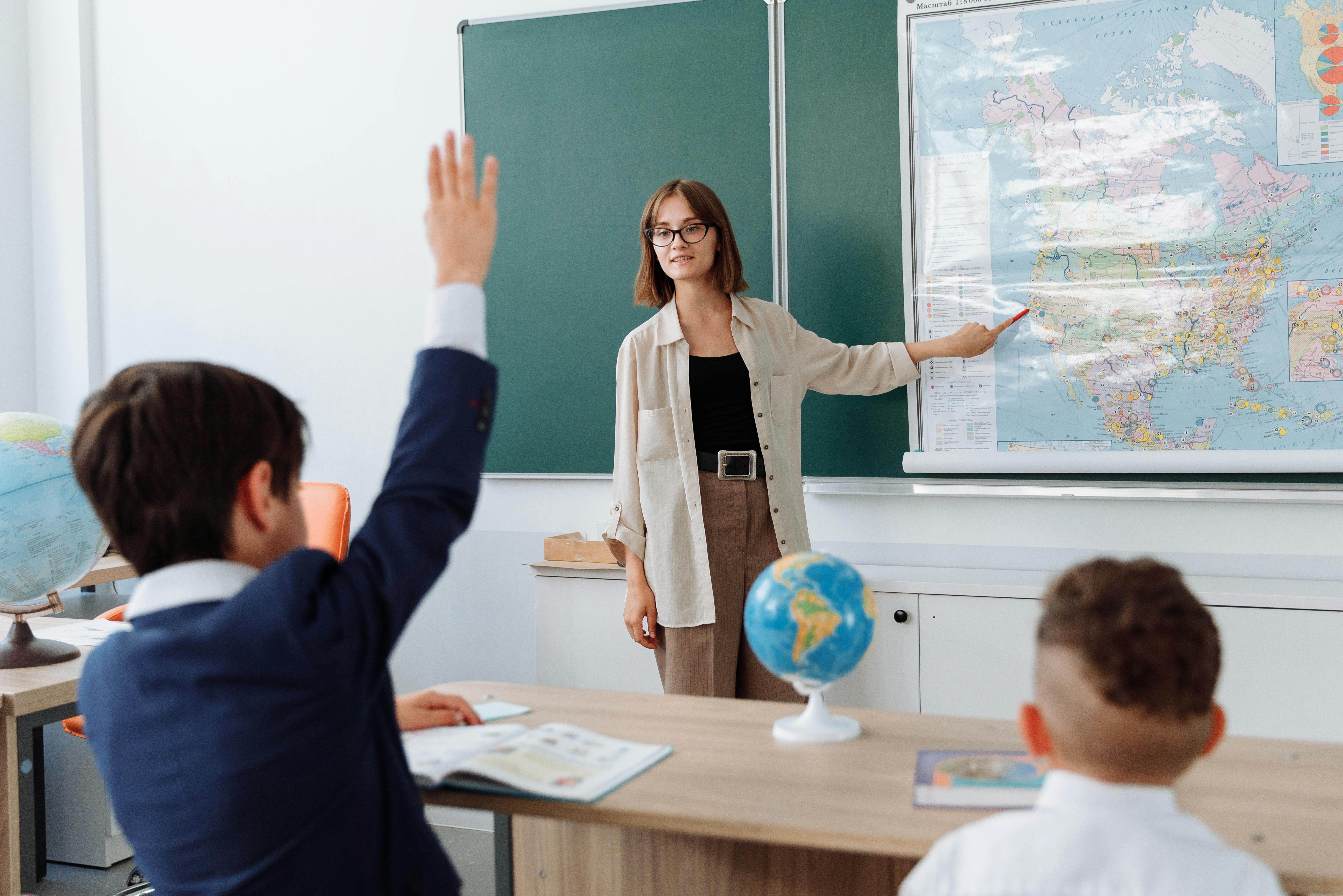 A woman teacher pointing at a map at the front of a classroom