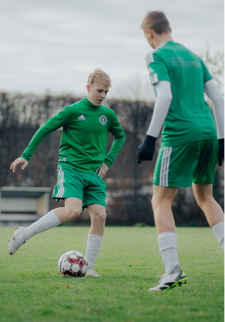 Two boys wearing a green football kit kicking a football