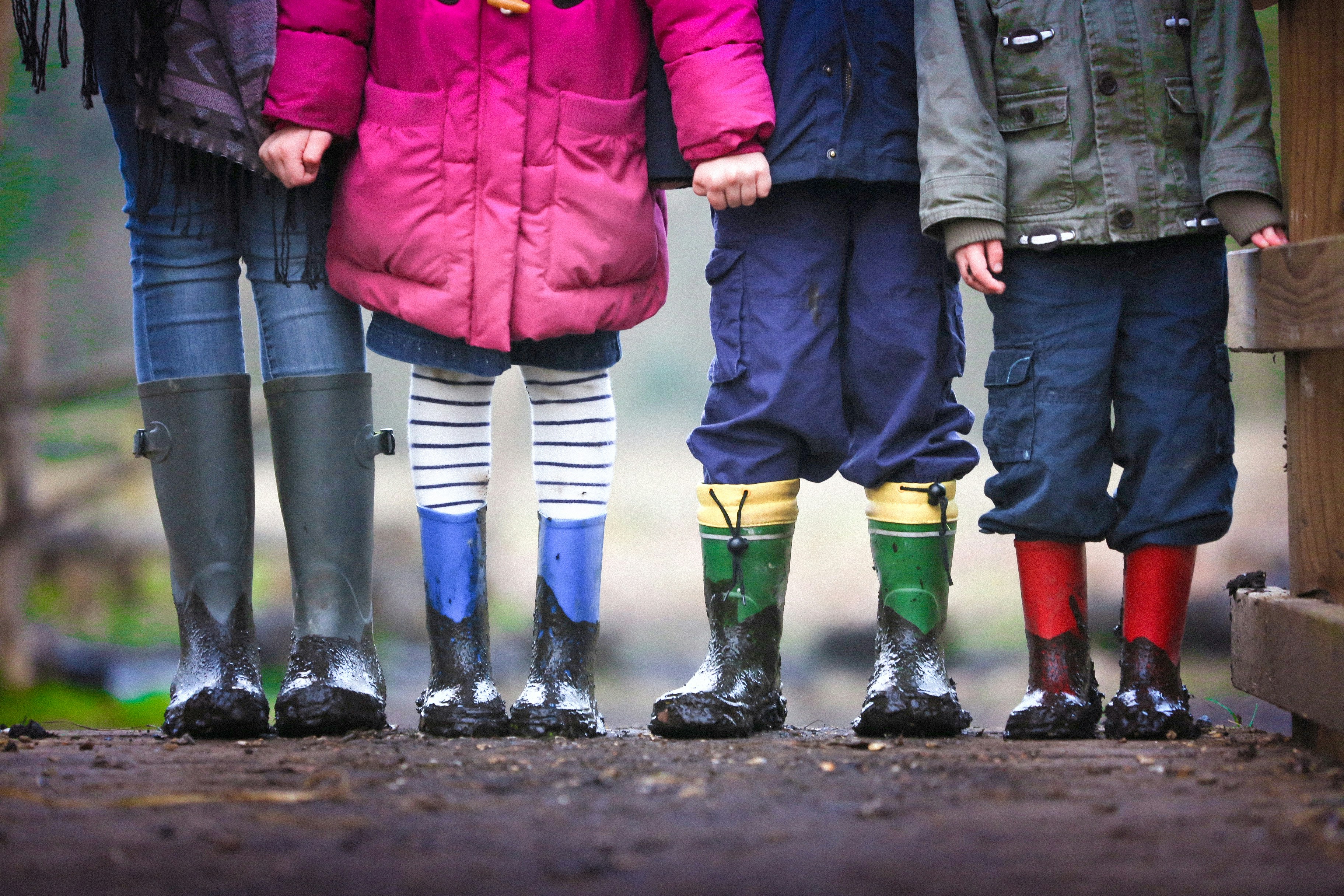 The bottom half of four young children wearing wellies