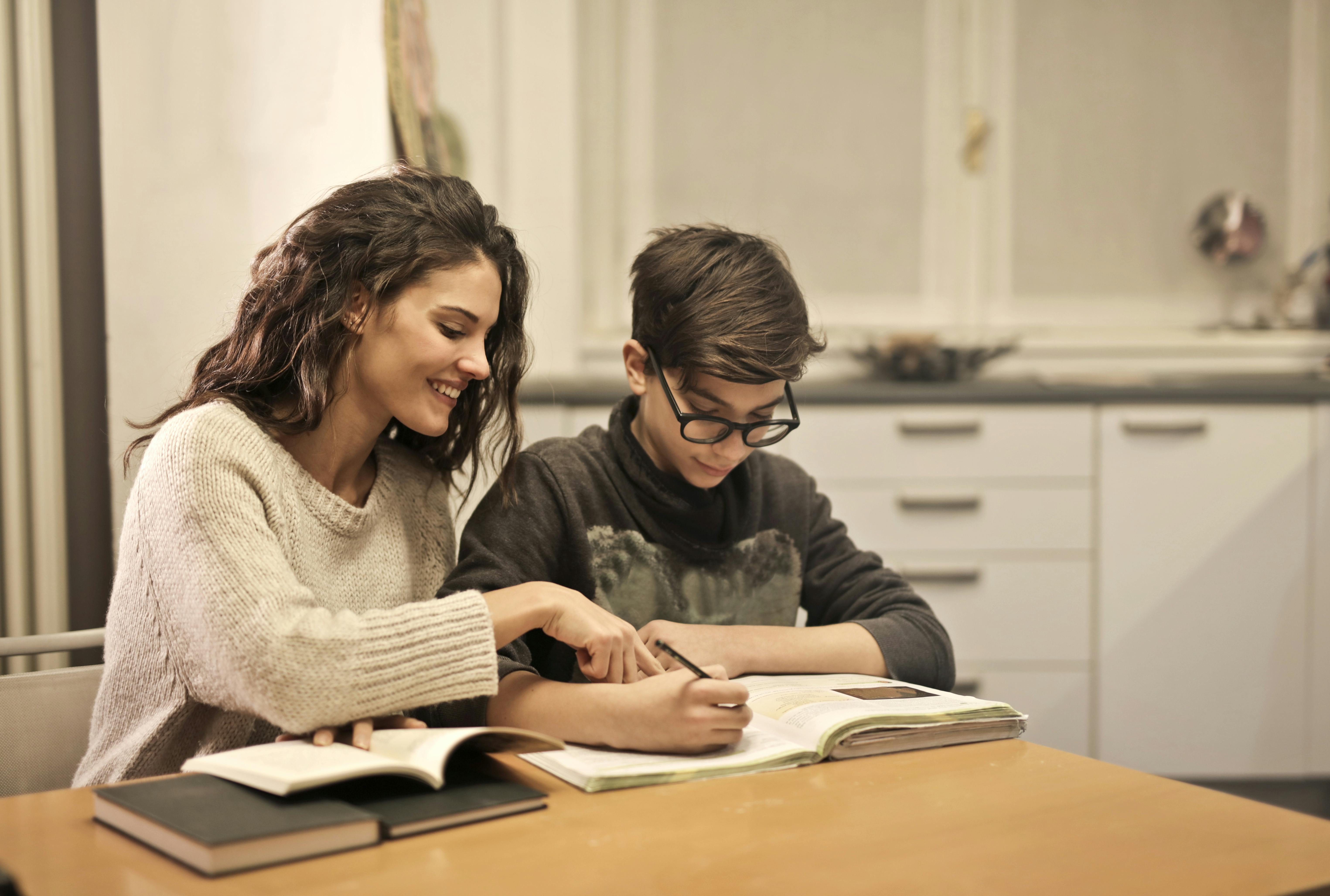 A woman and boy sat at a kitchen table doing work in a book